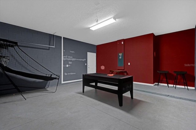 miscellaneous room featuring concrete block wall, baseboards, concrete flooring, and a textured ceiling