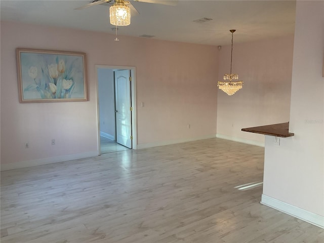 unfurnished living room with ceiling fan with notable chandelier and light wood-type flooring