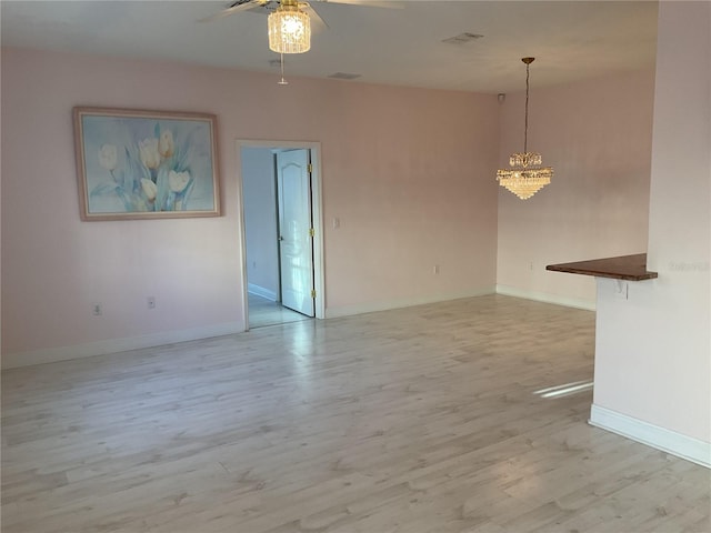 empty room featuring ceiling fan with notable chandelier and light hardwood / wood-style flooring