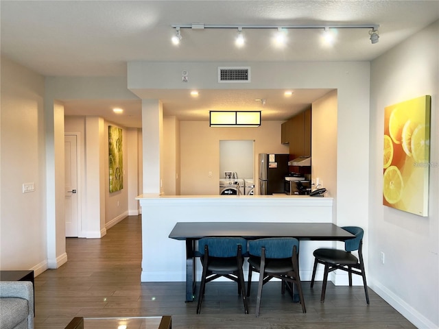 kitchen with track lighting, separate washer and dryer, dark hardwood / wood-style flooring, a breakfast bar area, and stainless steel refrigerator