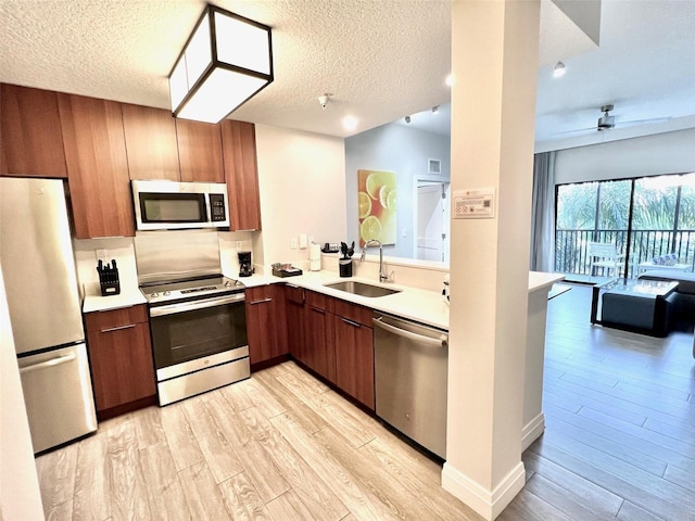 kitchen with a textured ceiling, stainless steel appliances, light hardwood / wood-style floors, and sink