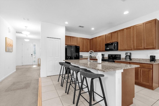 kitchen with light carpet, a kitchen breakfast bar, sink, black appliances, and an island with sink