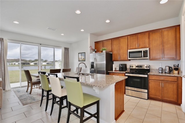 kitchen with light stone countertops, stainless steel appliances, sink, a center island with sink, and a breakfast bar area