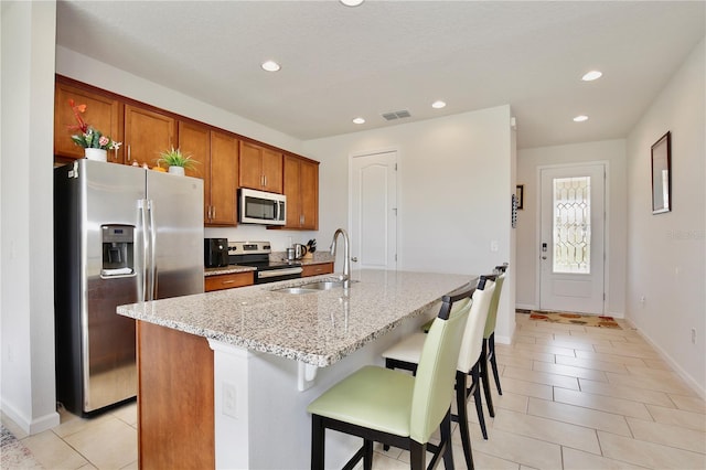 kitchen featuring sink, stainless steel appliances, light stone counters, an island with sink, and a breakfast bar