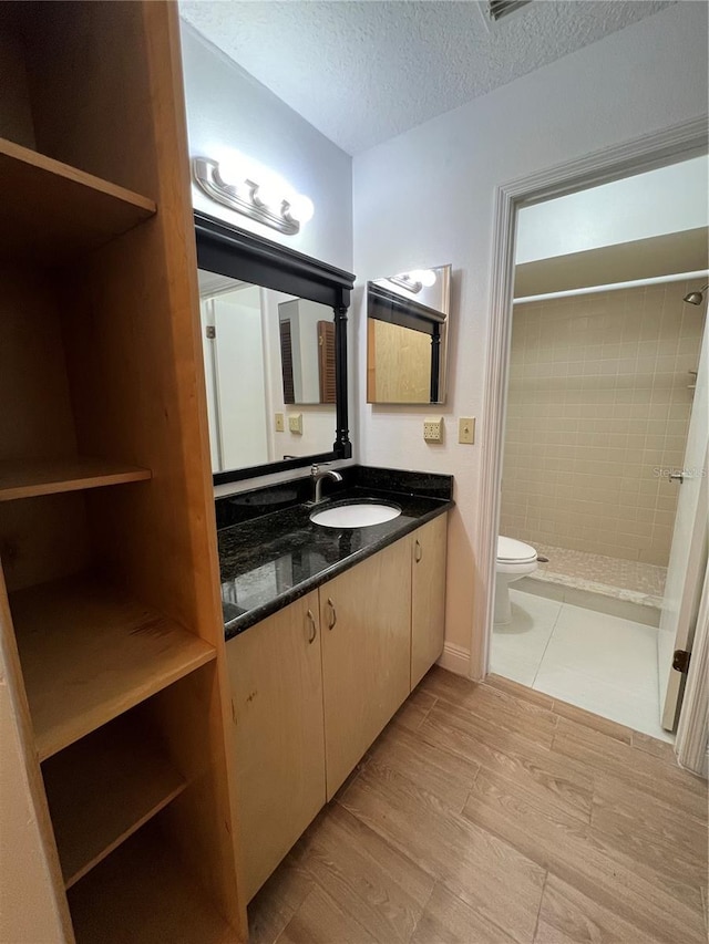 bathroom featuring vanity, a textured ceiling, tiled shower, hardwood / wood-style flooring, and toilet