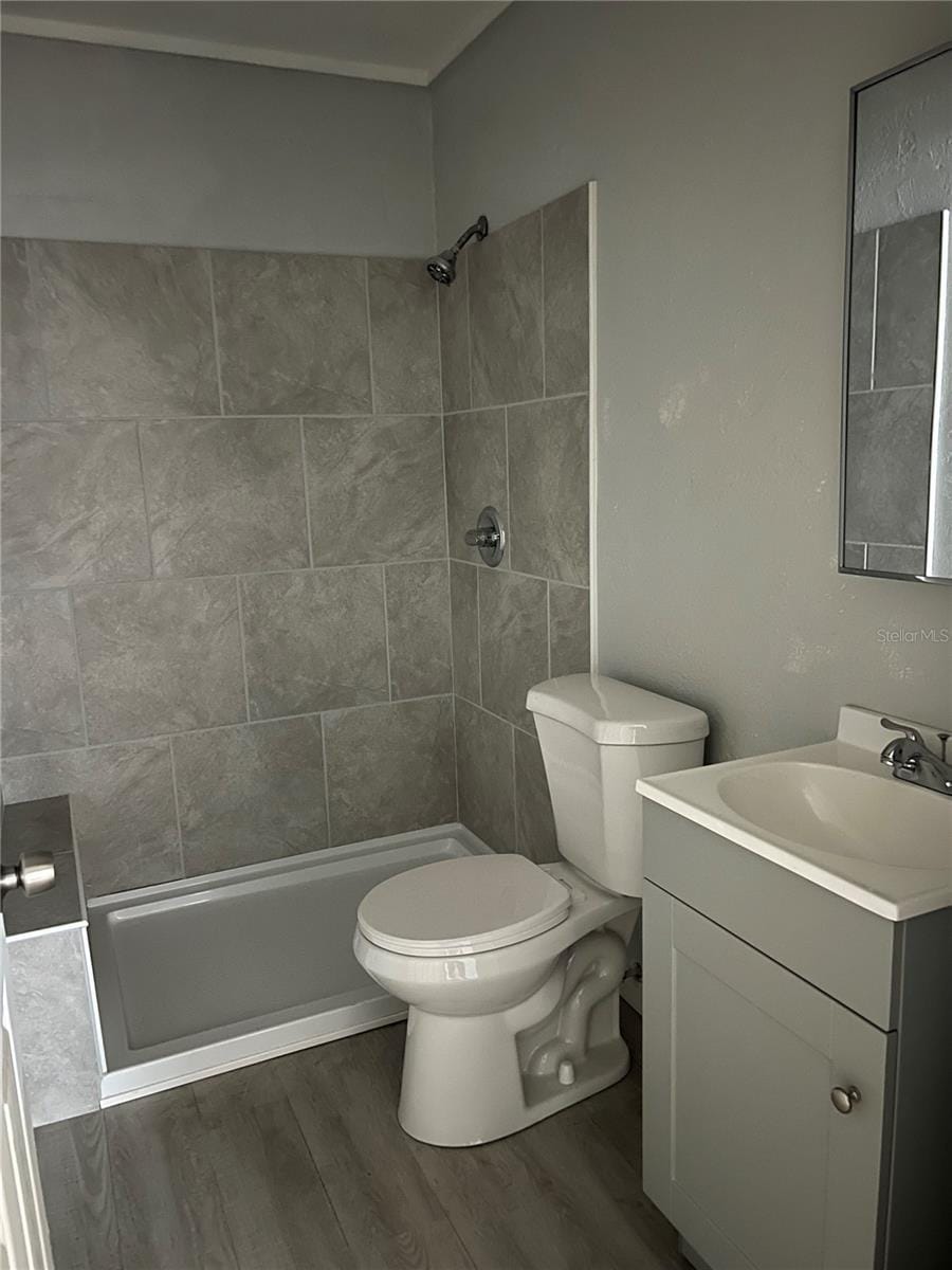 bathroom with vanity, toilet, hardwood / wood-style floors, and a tile shower