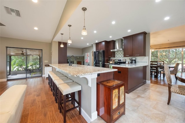 kitchen with pendant lighting, black fridge, plenty of natural light, and wall chimney exhaust hood