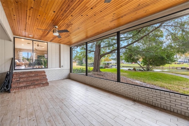 unfurnished sunroom with ceiling fan, a water view, and wooden ceiling