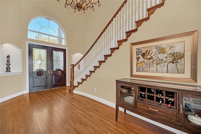 entrance foyer featuring hardwood / wood-style floors, a notable chandelier, french doors, and a high ceiling