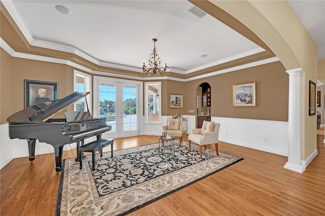 sitting room with ornate columns, light hardwood / wood-style flooring, a tray ceiling, crown molding, and french doors