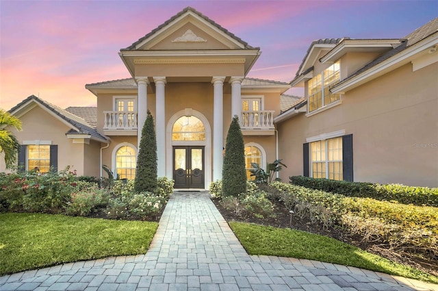 exterior entry at dusk with french doors and a balcony