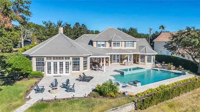 rear view of house featuring french doors, a patio, a pool with hot tub, and an outdoor fire pit