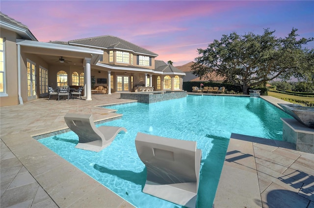 pool at dusk featuring a patio, area for grilling, and ceiling fan