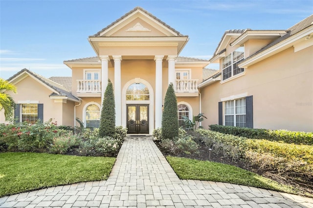 doorway to property featuring a balcony, a lawn, and french doors