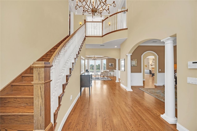 entryway featuring hardwood / wood-style flooring, a towering ceiling, a chandelier, and decorative columns