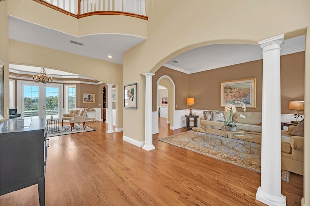 foyer with ornate columns, wood-type flooring, ornamental molding, and french doors