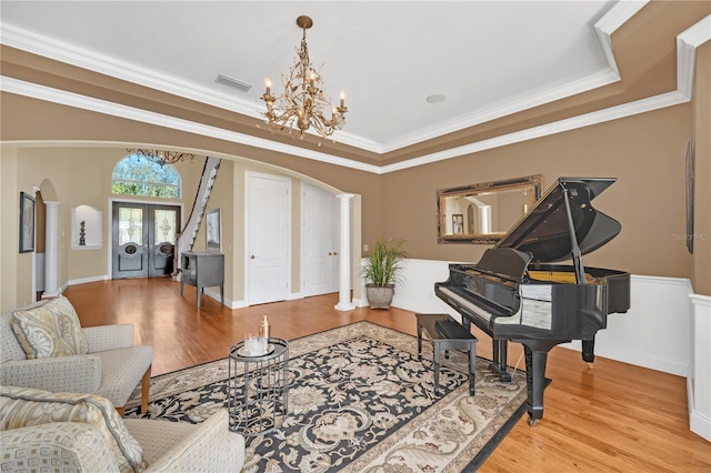 living area with crown molding, an inviting chandelier, light hardwood / wood-style floors, french doors, and ornate columns