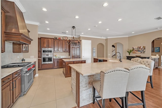 kitchen with premium range hood, stainless steel appliances, a kitchen breakfast bar, a spacious island, and decorative light fixtures