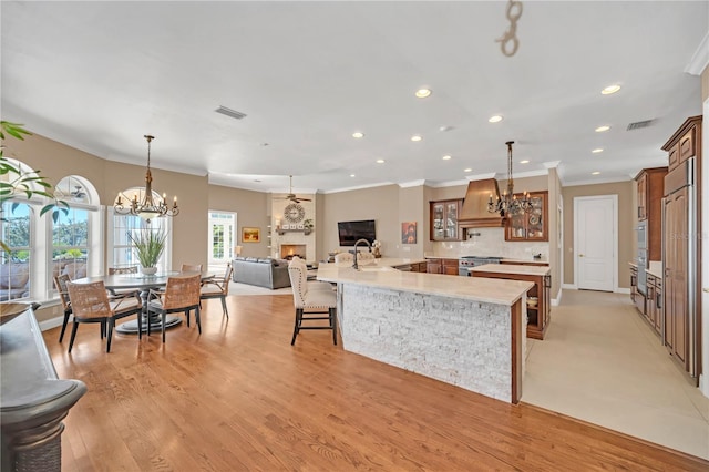 kitchen with a kitchen bar, hanging light fixtures, light wood-type flooring, stainless steel range, and custom range hood