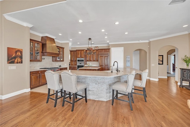 kitchen with a spacious island, a kitchen bar, custom exhaust hood, appliances with stainless steel finishes, and light hardwood / wood-style floors