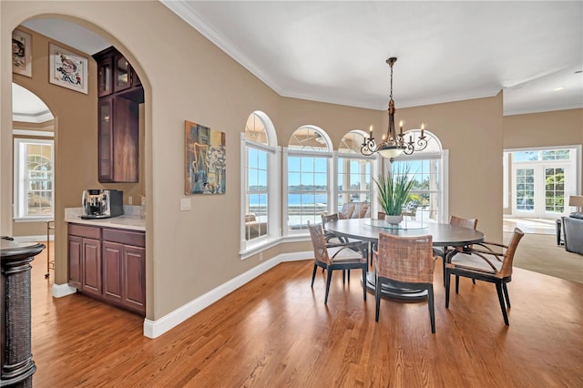 dining area featuring crown molding, a water view, a chandelier, and light hardwood / wood-style floors