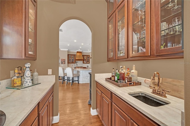 bar featuring sink, custom exhaust hood, ornamental molding, light stone counters, and light wood-type flooring