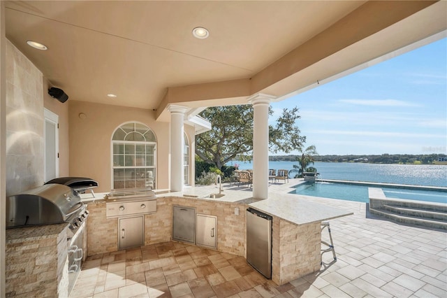 view of patio / terrace featuring area for grilling, a wet bar, a water view, and an outdoor kitchen