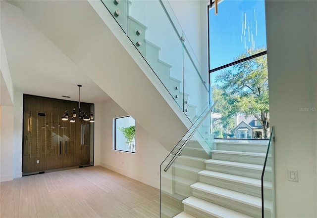 stairway with wood walls, a high ceiling, a wealth of natural light, and a chandelier