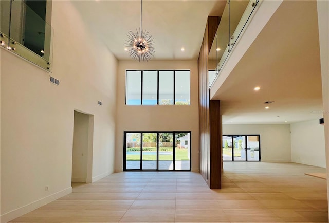 unfurnished living room featuring a chandelier, a high ceiling, and light hardwood / wood-style floors