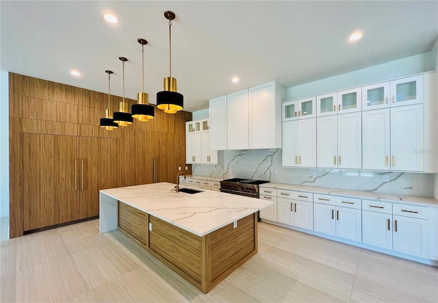 kitchen with light stone counters, an island with sink, pendant lighting, decorative backsplash, and white cabinets