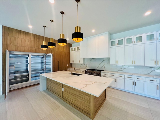 kitchen featuring light stone countertops, sink, hanging light fixtures, a kitchen island with sink, and white cabinets