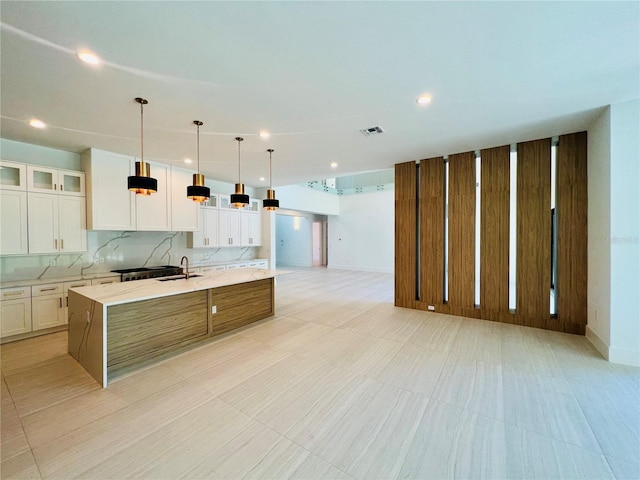 kitchen with light stone counters, a spacious island, sink, decorative light fixtures, and white cabinetry