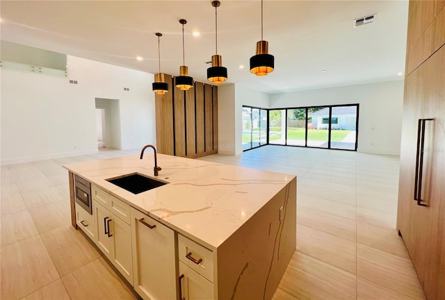 kitchen featuring light stone countertops, sink, a large island with sink, pendant lighting, and stainless steel microwave