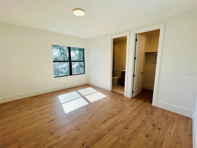 unfurnished bedroom with ensuite bath, a spacious closet, a closet, and light hardwood / wood-style floors