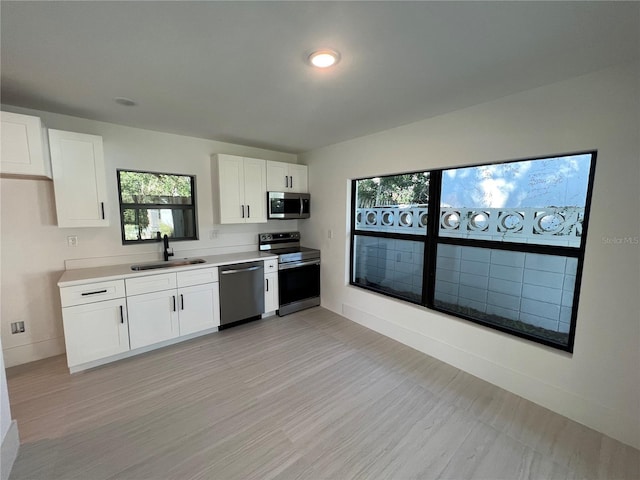 kitchen with light hardwood / wood-style floors, white cabinetry, sink, and appliances with stainless steel finishes