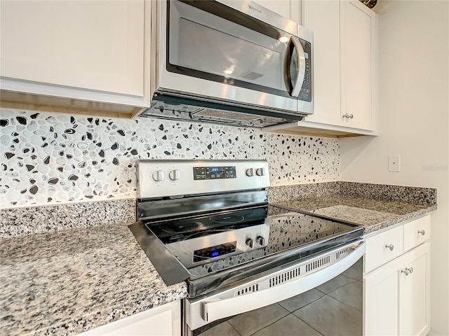 kitchen with tile patterned floors, stainless steel appliances, light stone countertops, decorative backsplash, and white cabinets