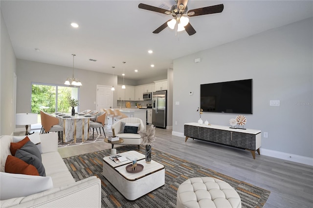 living room with ceiling fan with notable chandelier and hardwood / wood-style flooring