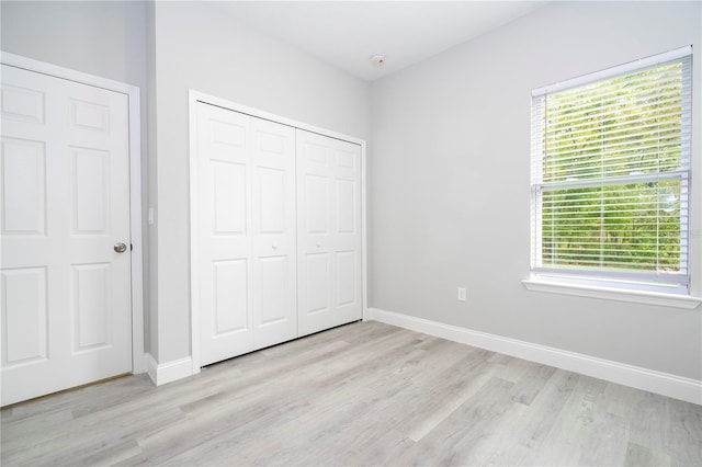 unfurnished bedroom featuring a closet, light hardwood / wood-style floors, and multiple windows