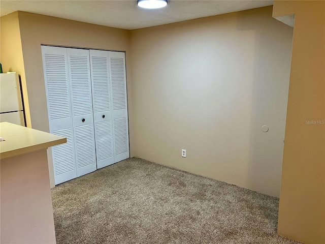 unfurnished bedroom with carpet flooring, a closet, and white refrigerator