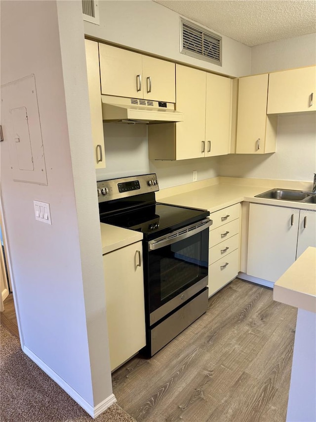 kitchen with a textured ceiling, under cabinet range hood, a sink, visible vents, and electric stove