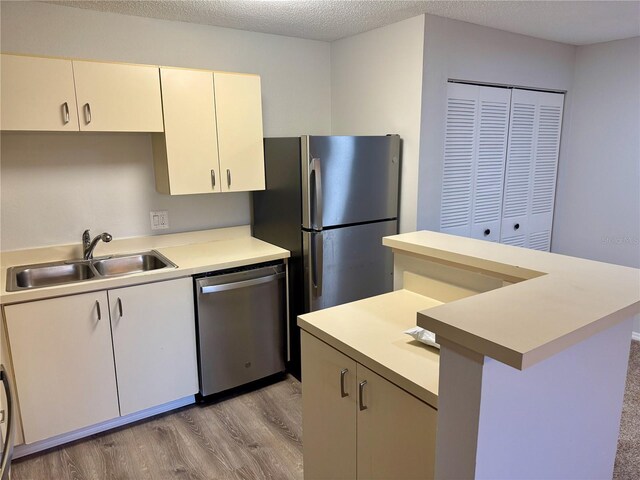 kitchen featuring a textured ceiling, stainless steel appliances, a sink, light wood-style floors, and light countertops