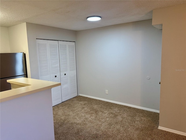 unfurnished bedroom featuring a textured ceiling, carpet flooring, baseboards, a closet, and freestanding refrigerator