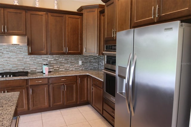 kitchen featuring black gas stovetop, stainless steel refrigerator with ice dispenser, decorative backsplash, light stone countertops, and extractor fan