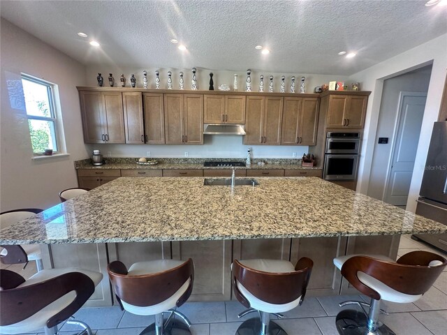 kitchen with a textured ceiling, stainless steel appliances, a large island, a breakfast bar area, and light tile patterned flooring