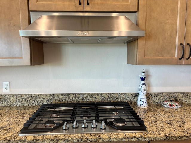 details featuring stainless steel gas cooktop, dark stone countertops, and wall chimney range hood