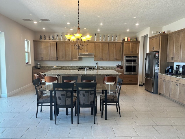 kitchen with a center island with sink, a kitchen bar, light stone countertops, and appliances with stainless steel finishes