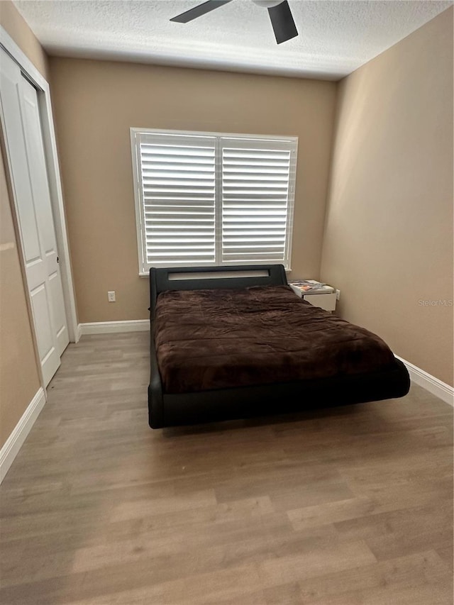 bedroom with ceiling fan, a closet, light hardwood / wood-style floors, and a textured ceiling