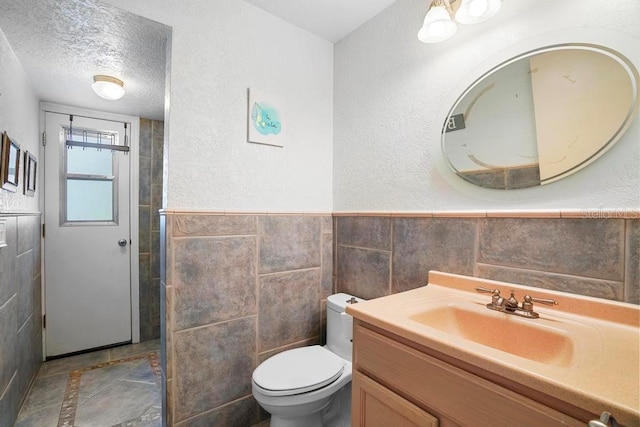 bathroom with vanity, a textured ceiling, toilet, and tile walls