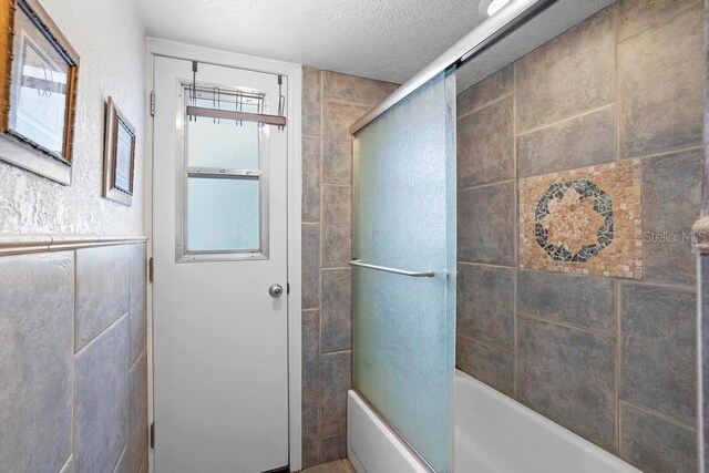 bathroom featuring a textured ceiling and combined bath / shower with glass door