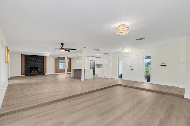 unfurnished living room with ceiling fan with notable chandelier, light hardwood / wood-style floors, and a brick fireplace